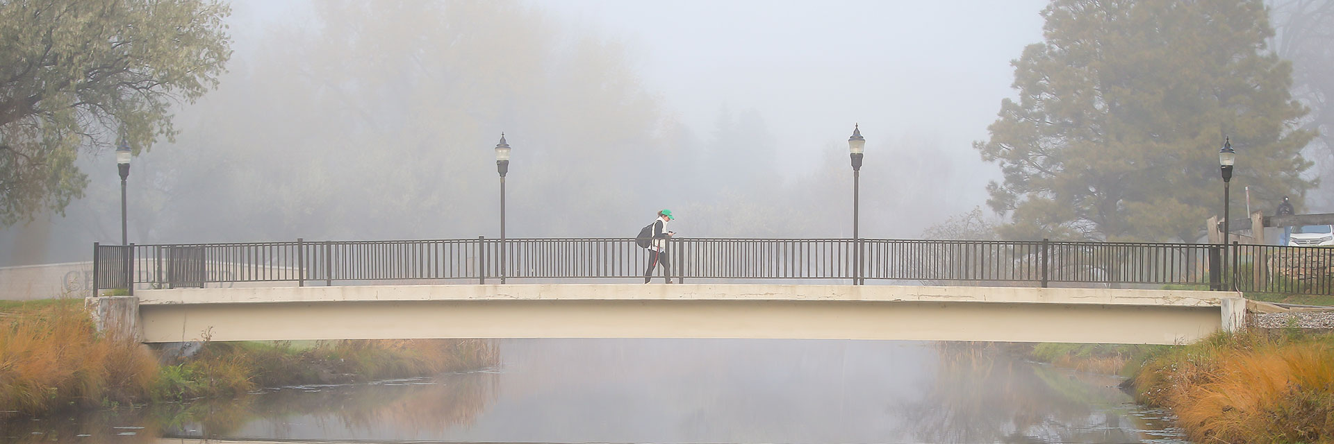 A student walking across a bridge on a foggy morning.