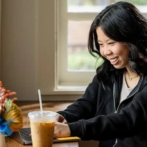 A young woman working on her laptop in a coffee shop, smiling.