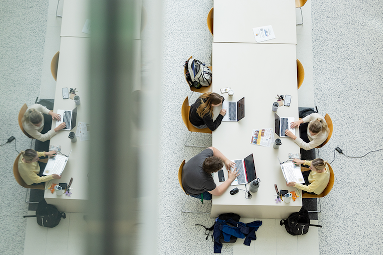 Aerial photo of studetns sitting at long tables working on their computers. 