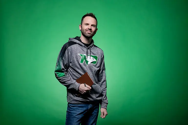 Austin standing in front of green screen with UND Fighting Hawks sweatshirt