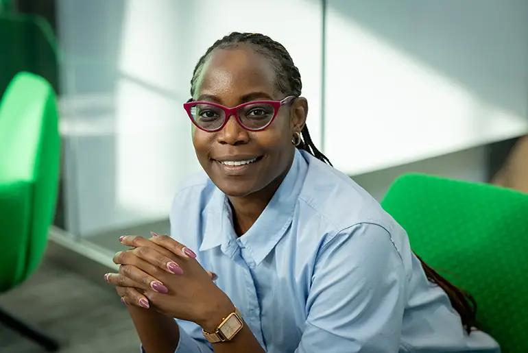 Imelda wearing red glasses with her hands clasped, smiling at the camera