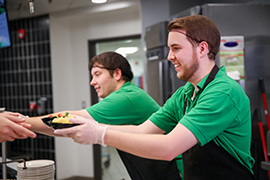student employee passing bowl of food