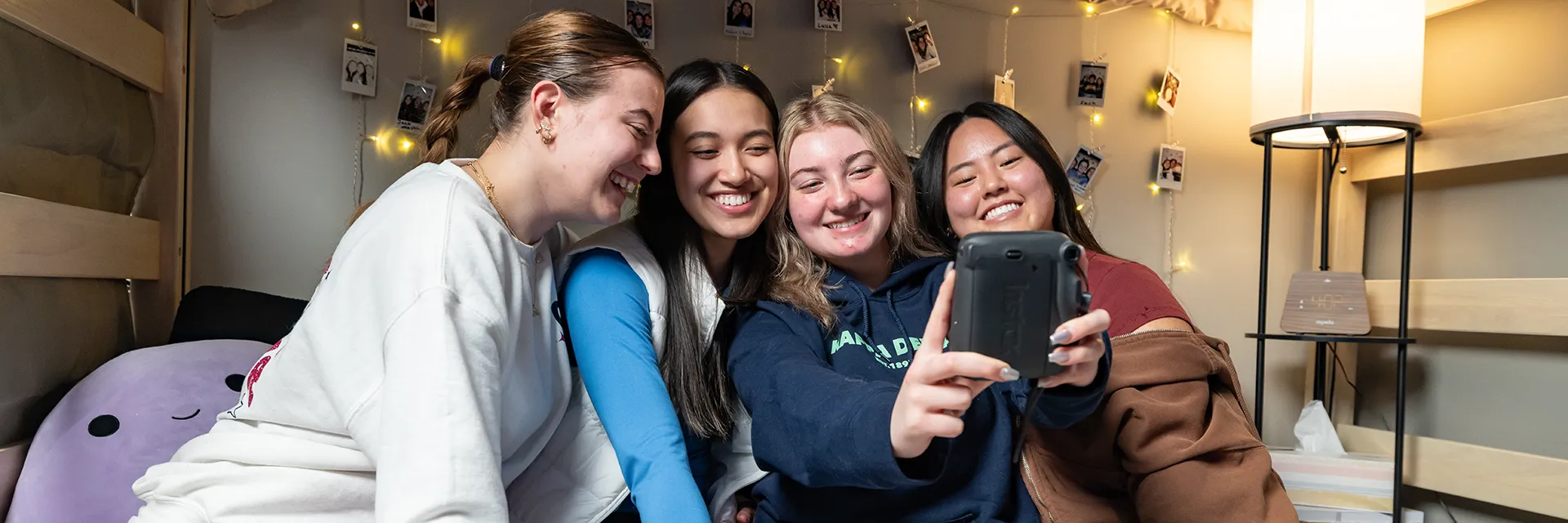 4 female UND Students Sitting Together in Their Dorm Room taking a selfie on a cell phone