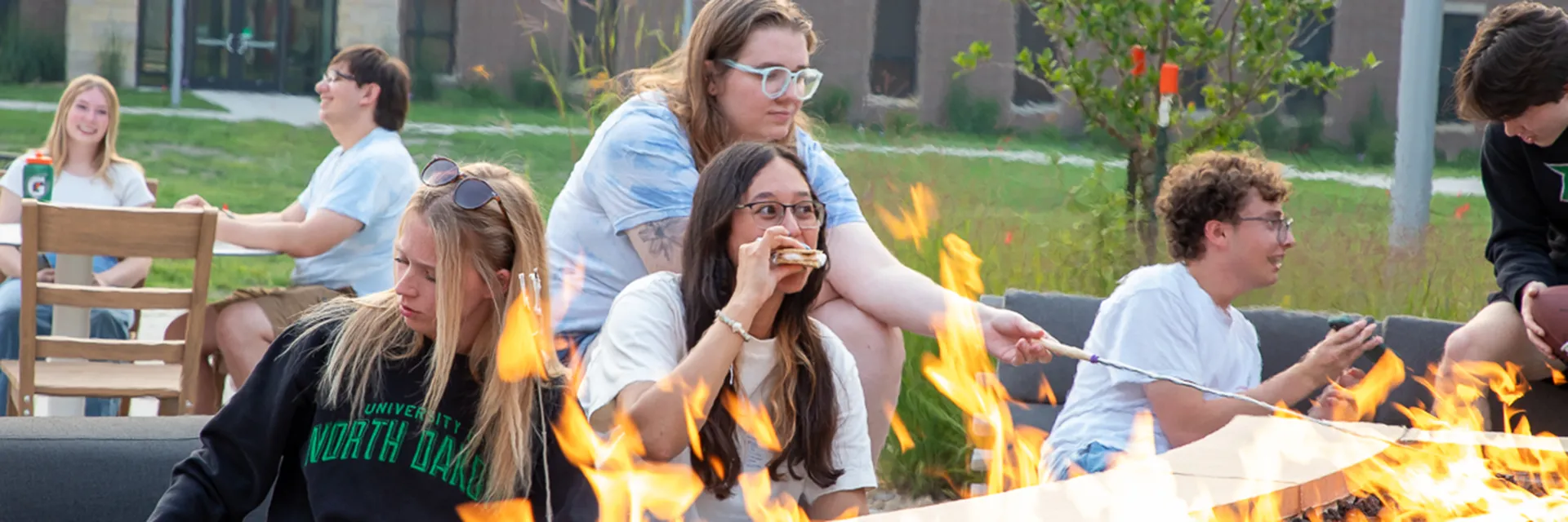 Students socialize around an outdoor firepit and make s'mores