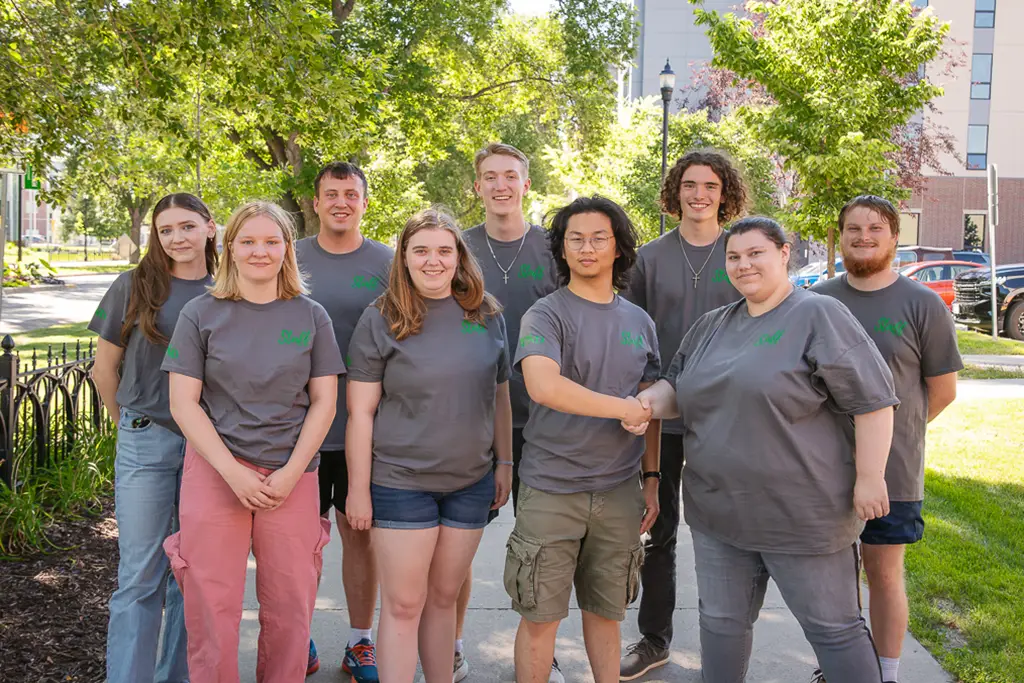 Group of young people pose for a photo with the side walk continuing behind them