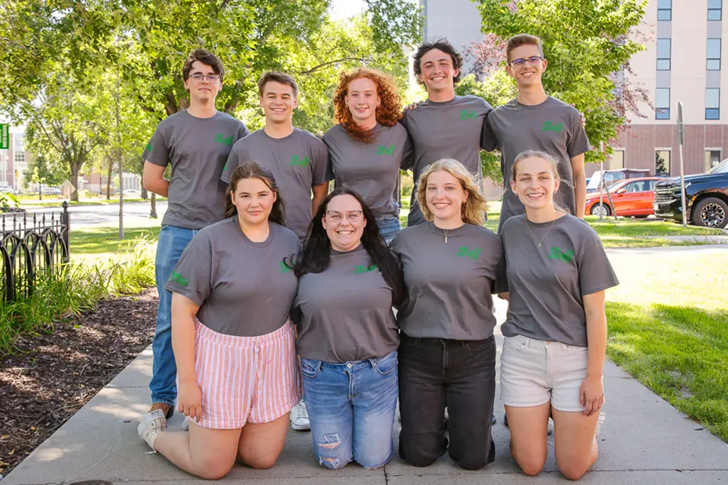 Group of young people pose for a photo with the side walk continuing behind them