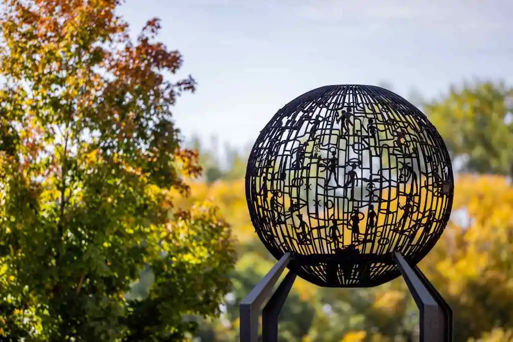 Ornate metal sphere sculpture amidst autumn trees.