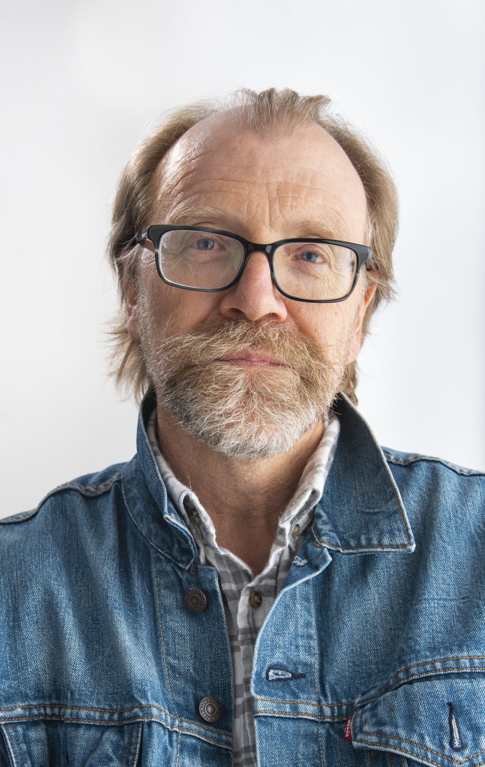 Photograph of novelist George Saunders, wearing a denim jacket over a button-down shirt. Photo credit: Zach Krahmer